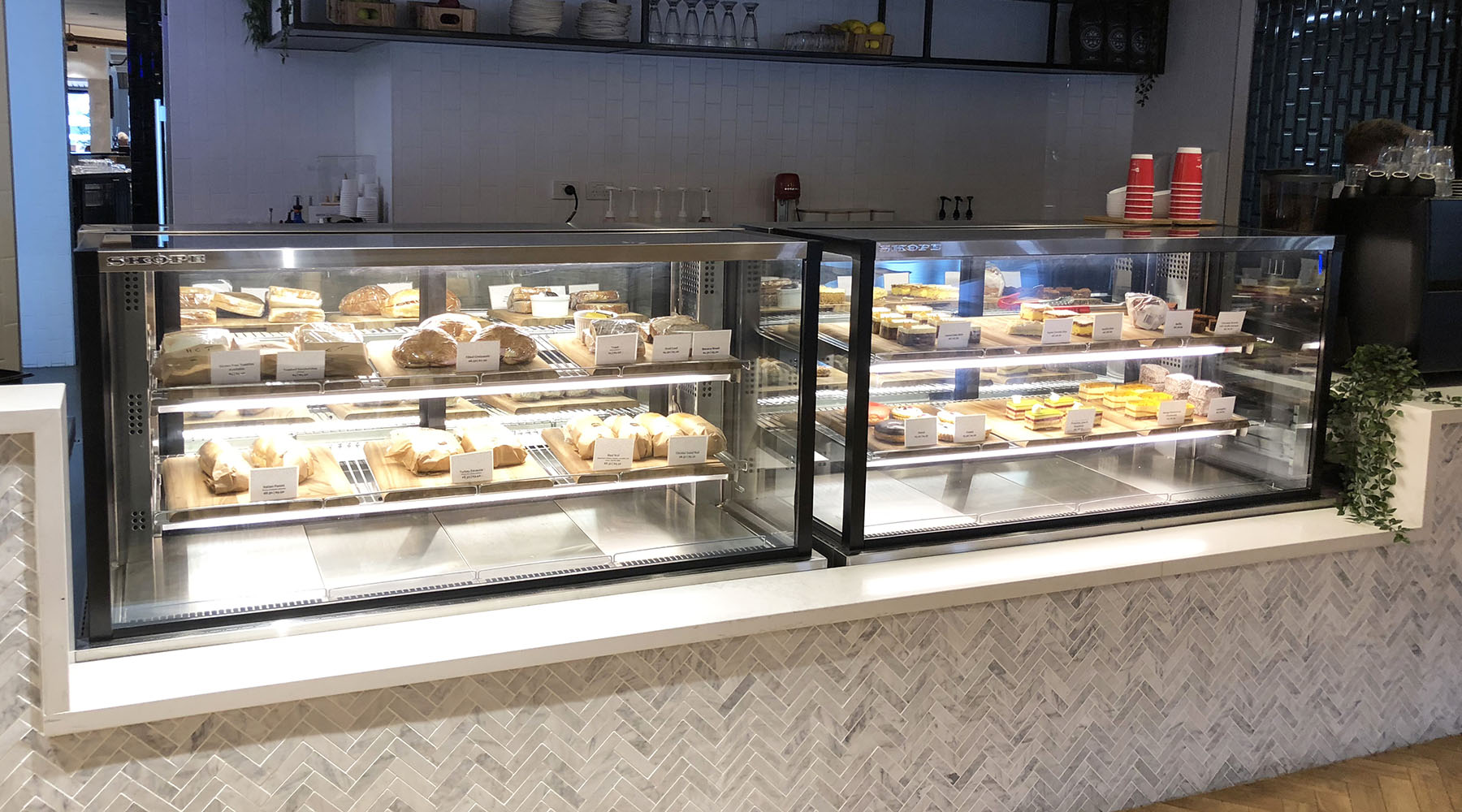 Two glass display cabinets of bread and cakes on a cafe counter