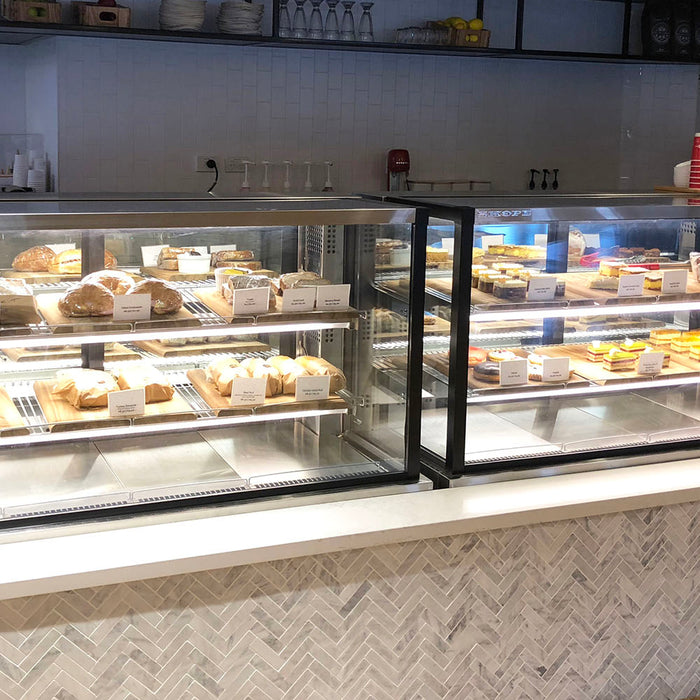 Two glass display cabinets of bread and cakes on a cafe counter