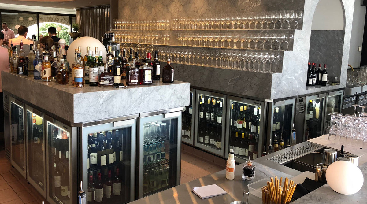 Glass door bar fridges built in under a marble-topped bar, stocked with wine and drinks