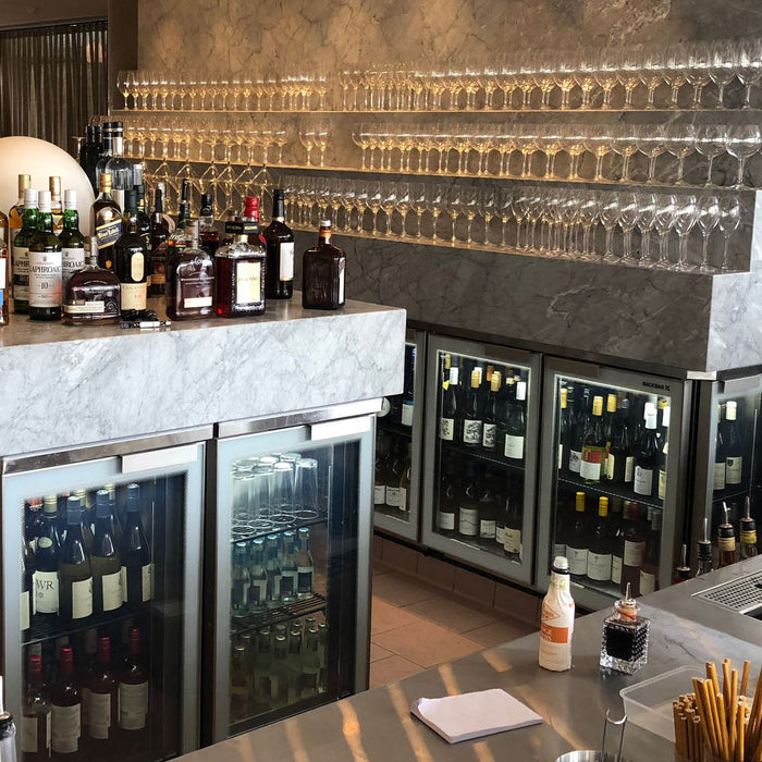 Glass door bar fridges built in under a marble-topped bar, stocked with wine and drinks