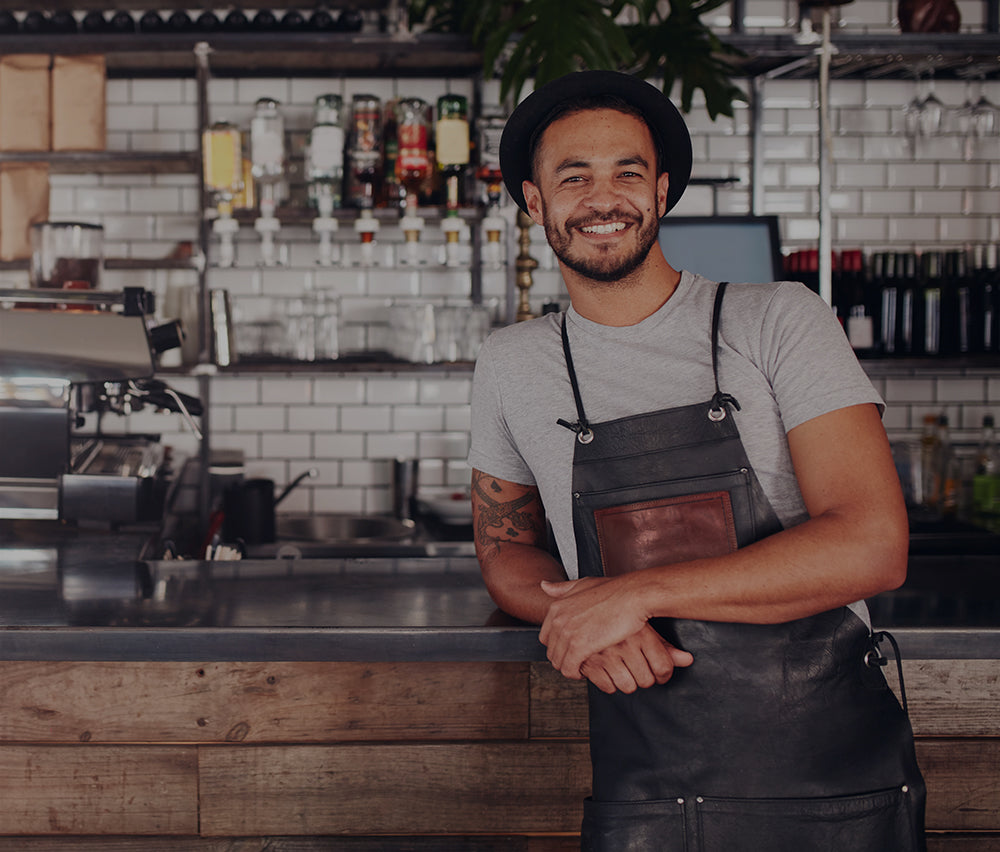 A cafe owner in an apron, smiling at his counter